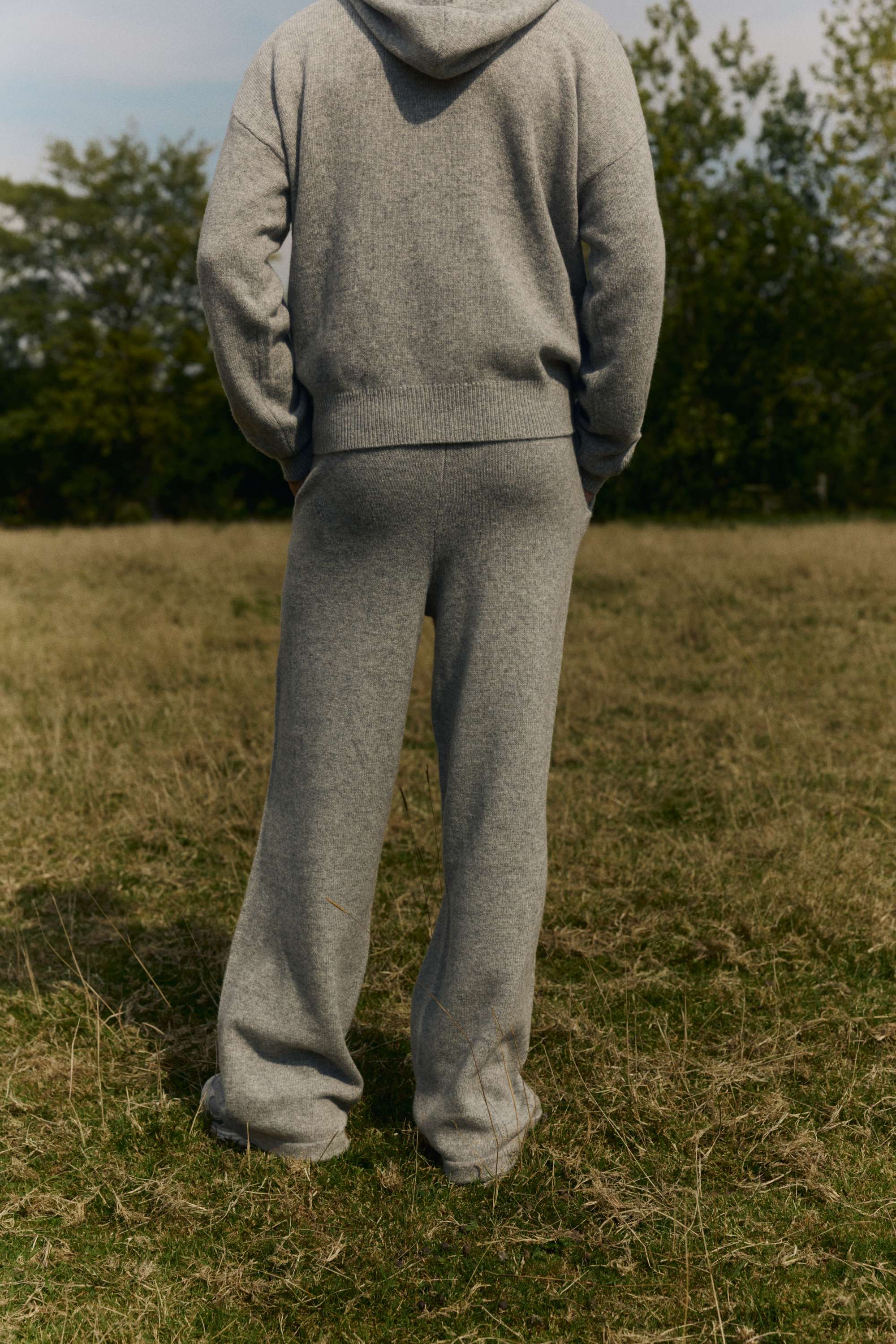 Back view of a man wearing CASPARA grey melange woolknit straight leg pants and a matching hoodie outdoors.
